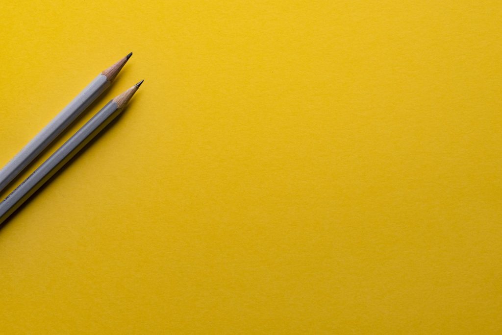 Two gray pencils on yellow surface