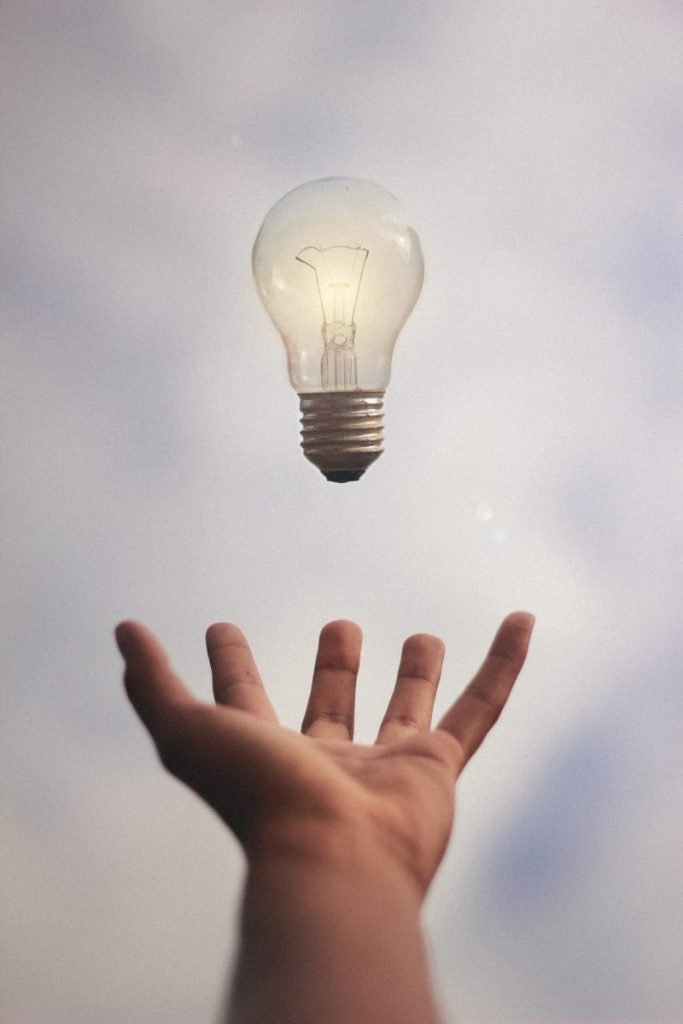 Light bulb floats in the air above a hand.