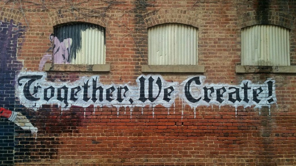 "Together we create" graffiti-ed on a brick wall
