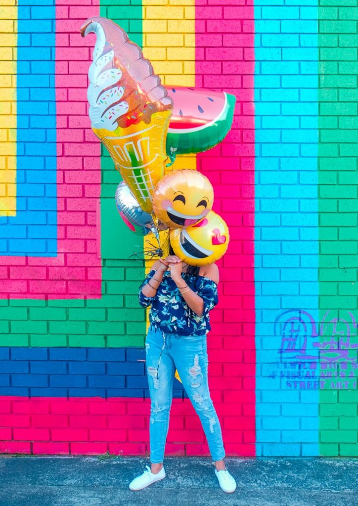 Person holding balloons shaped like emoticons against a brightly painted wall